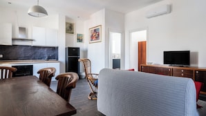 Un salon moderne avec un canapé, une table à manger et des chaises. Il y a un coin cuisine équipé d’un réfrigérateur, d’une cuisinière et d’un évier. Un téléviseur est fixé sur un meuble en bois.