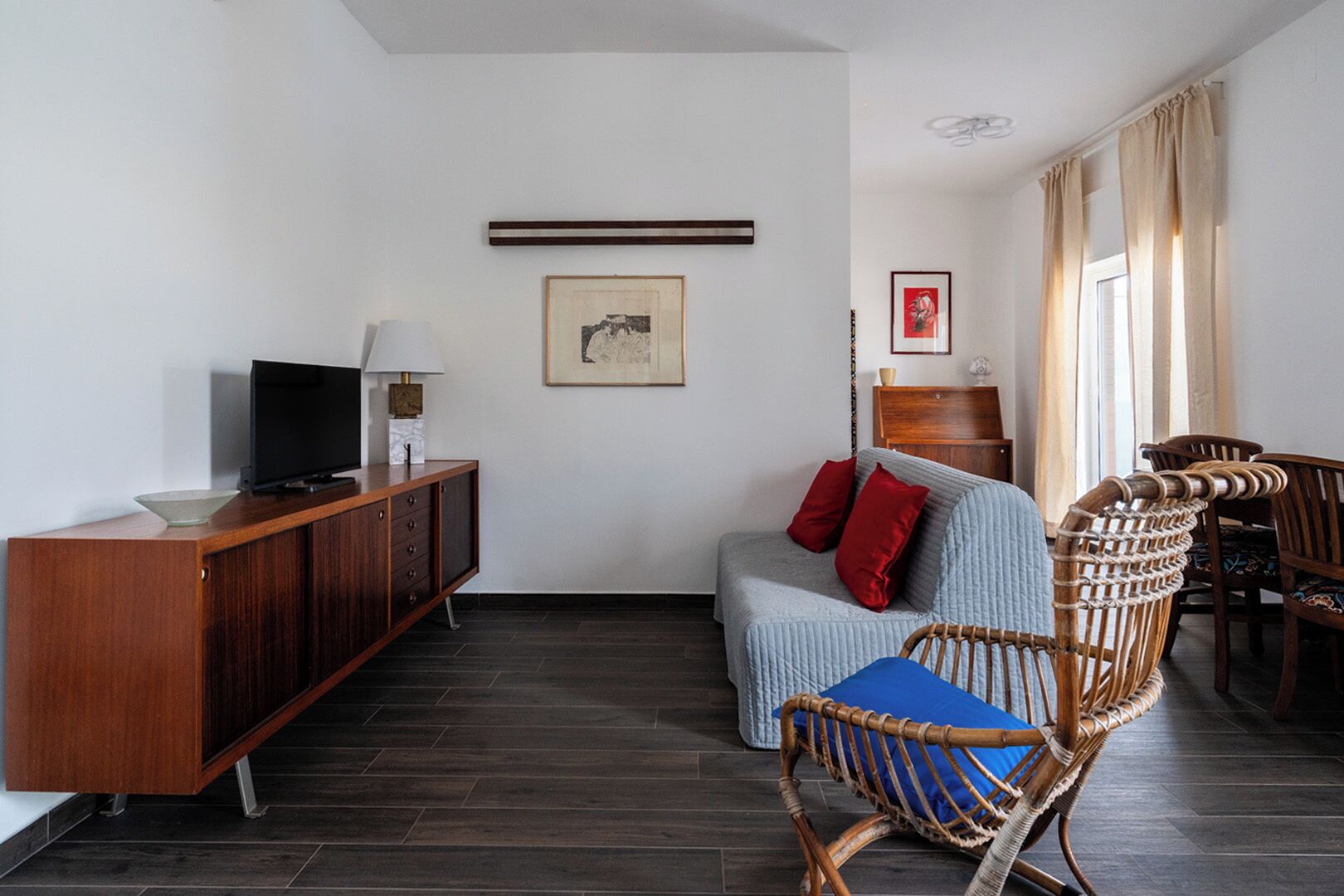 Un soggiorno moderno con un mobile in legno, una televisione, un quadro incorniciato, un divano con cuscini e poltrone in vimini.