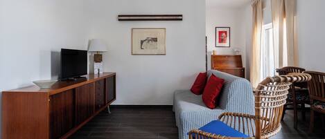 Un soggiorno moderno con un mobile in legno, una televisione, un quadro incorniciato, un divano con cuscini e poltrone in vimini.