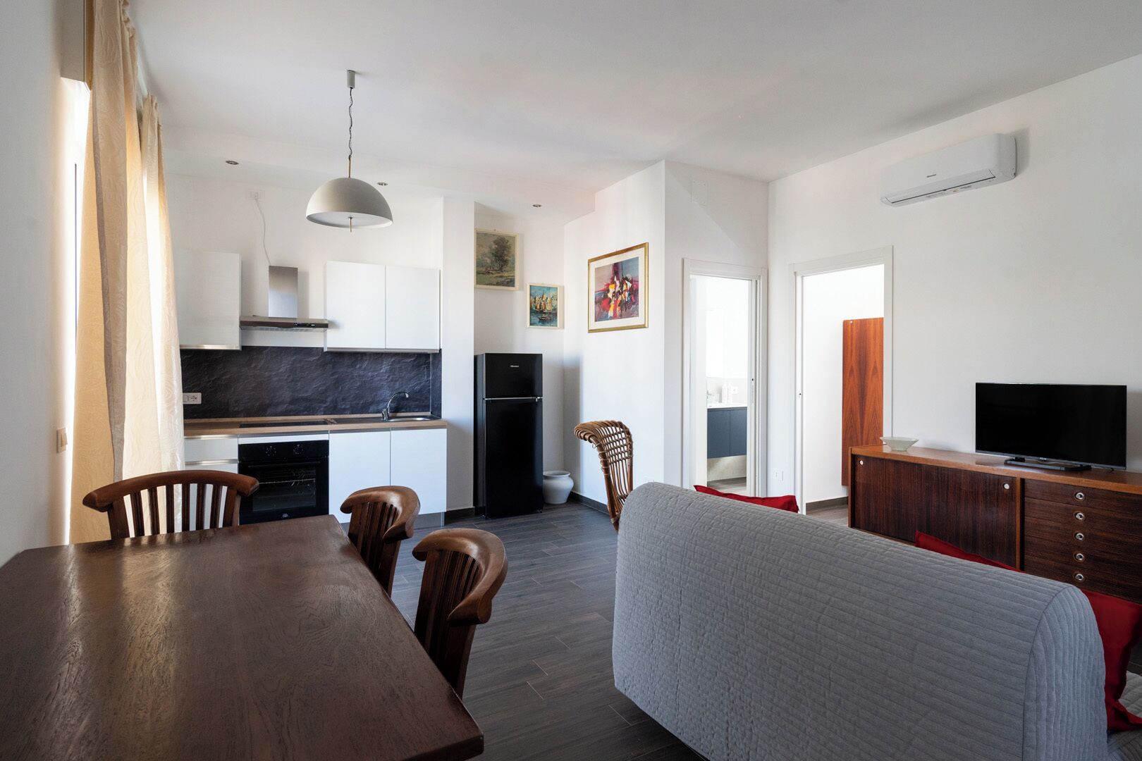 A modern kitchen with a built-in oven, a black refrigerator, and a dining area with a wooden table and chairs.