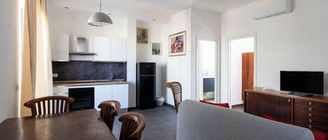 A modern kitchen with a built-in oven, a black refrigerator, and a dining area with a wooden table and chairs.