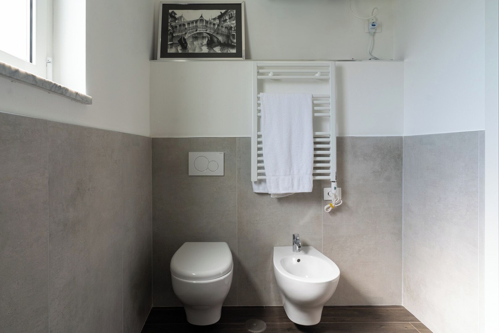 Une salle de bain équipée de toilettes, d’un bidet, d’un porte-serviettes et d’un tableau encadré au mur.