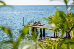Een houten steiger die zich uitstrekt over kalm water, met twee ligstoelen en een lantaarnpaal.