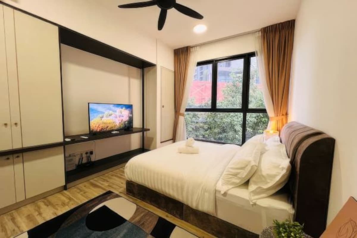 A bedroom with a bed, a TV on a stand, a window with curtains, and a ceiling fan.