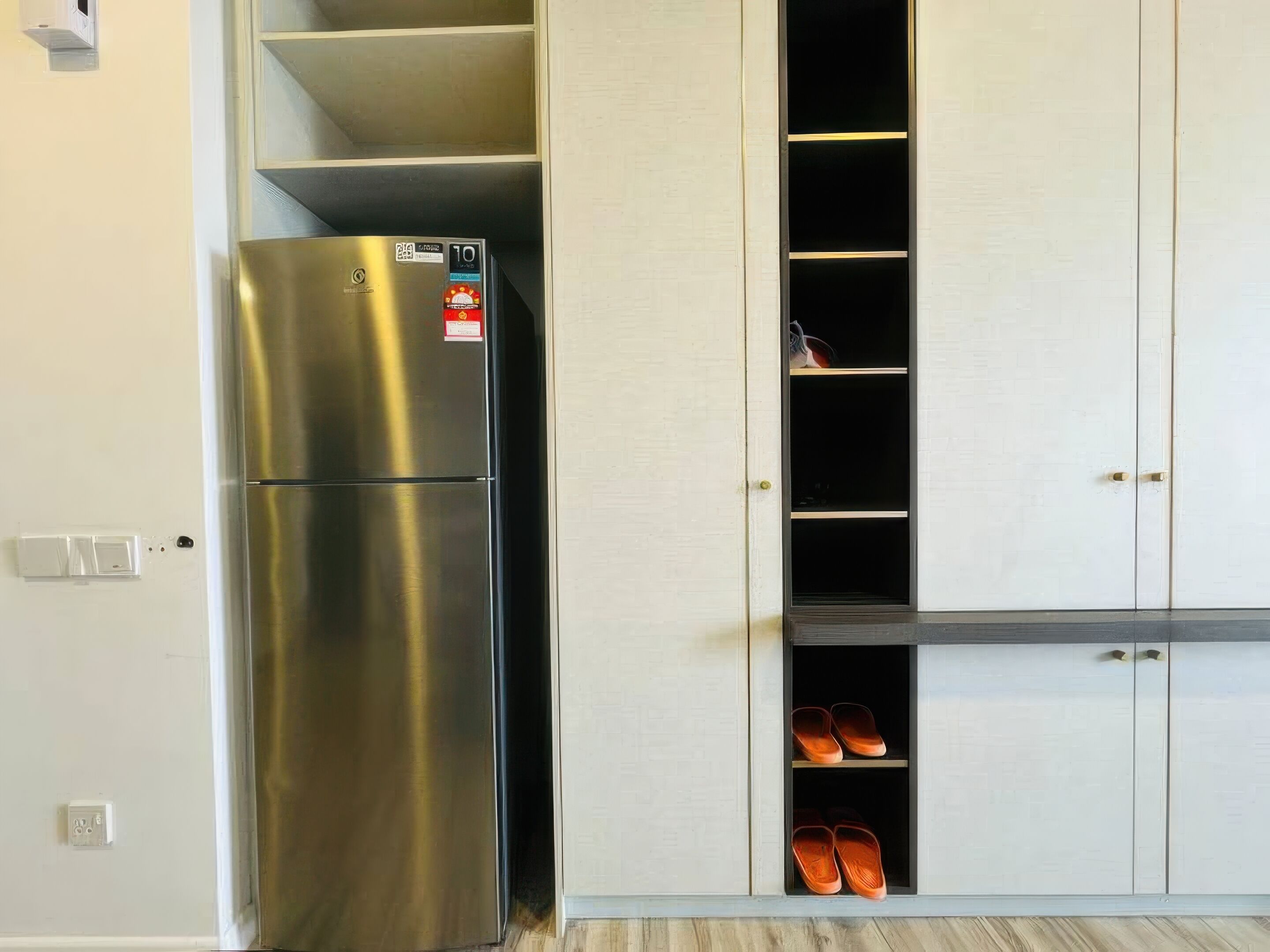 A kitchen with a stainless steel refrigerator, white cabinets, and a shoe rack.