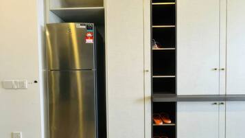 A kitchen with a stainless steel refrigerator, white cabinets, and a shoe rack.
