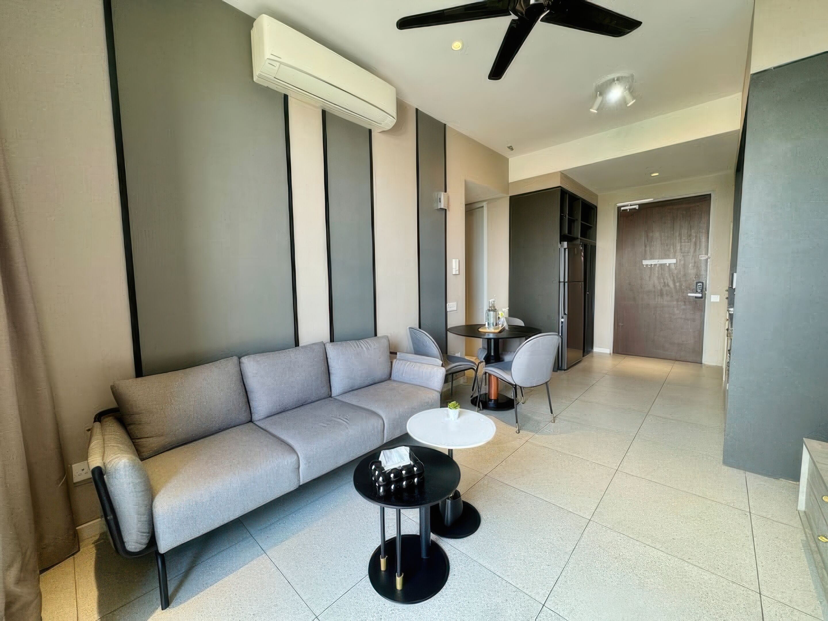 Ein modernes Wohnzimmer mit einem grauen Sofa, einem kleinen runden Tisch und einem Deckenventilator.