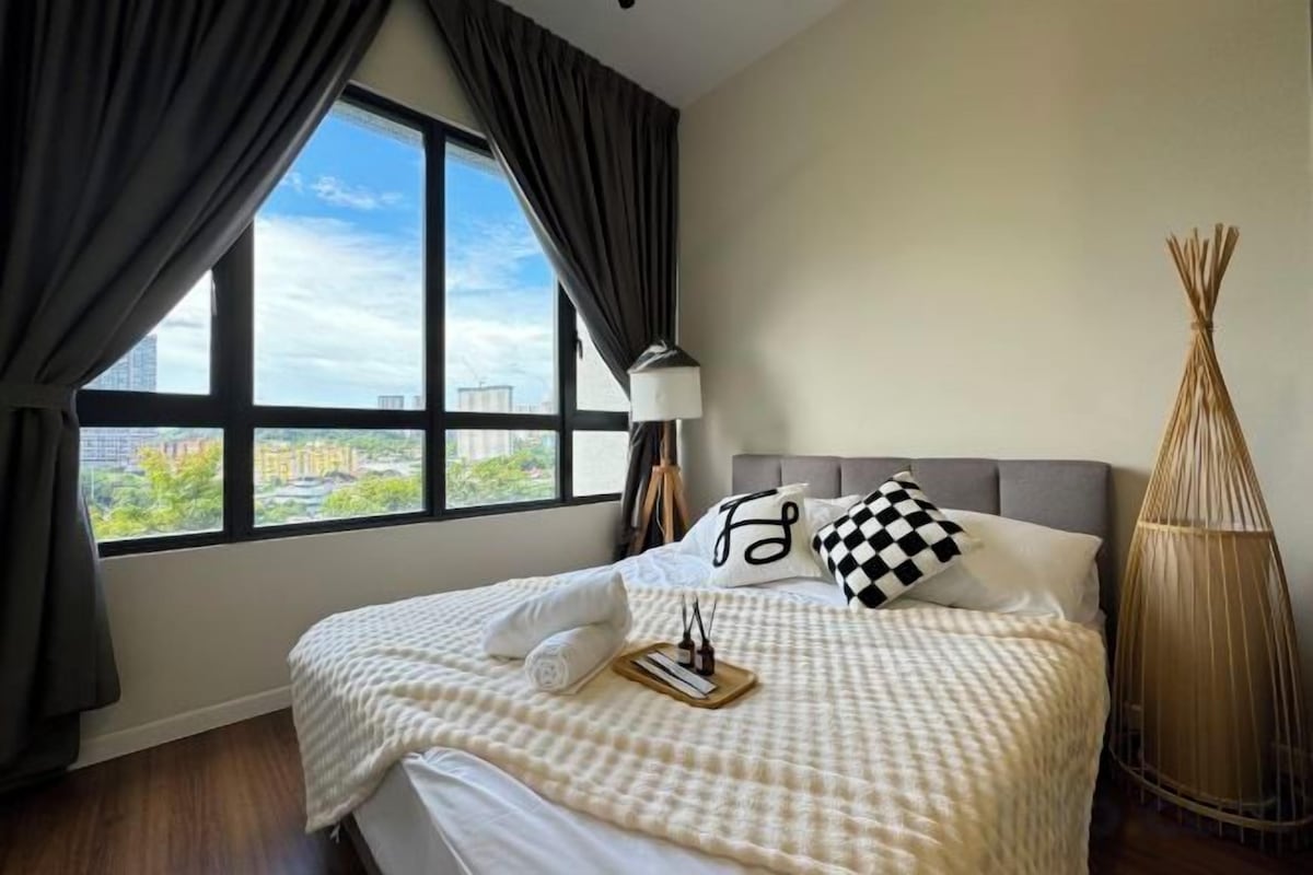 A hotel room with a large window, a bed with checkered bedding, and a decorative lamp.