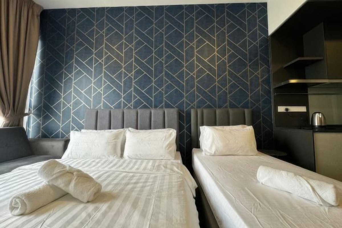 A hotel room with two beds, a grey headboard, and a patterned wall.