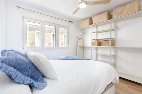A bedroom with a bed, a ceiling fan, a window, and built-in shelving with baskets.