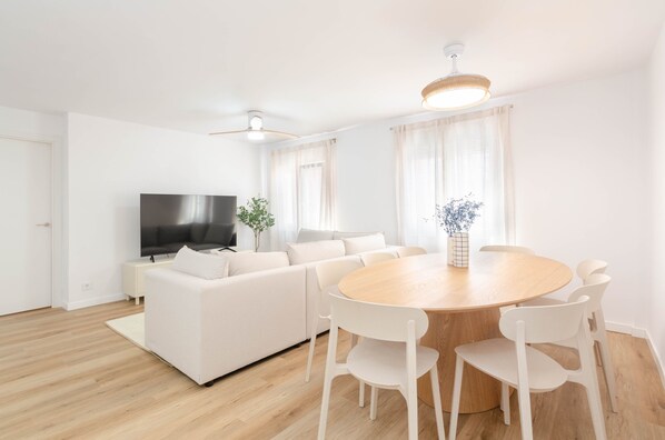 Un salon moderne comprenant un canapé, un téléviseur, une table à manger avec des chaises et une plante.