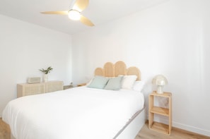 Une chambre à coucher comprenant un lit, un ventilateur de plafond, une table de chevet avec une lampe et un petit meuble.
