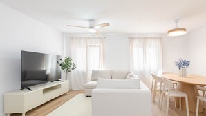 A modern living room with a flat-screen TV, a sofa, a dining table with chairs, and a ceiling fan. - Apartment 'Bilua' with Wi-Fi and Air Conditioning (Luanco)