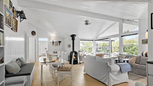 Un salon spacieux doté d’une cheminée, de meubles blancs et de grandes fenêtres donnant sur un paysage verdoyant.