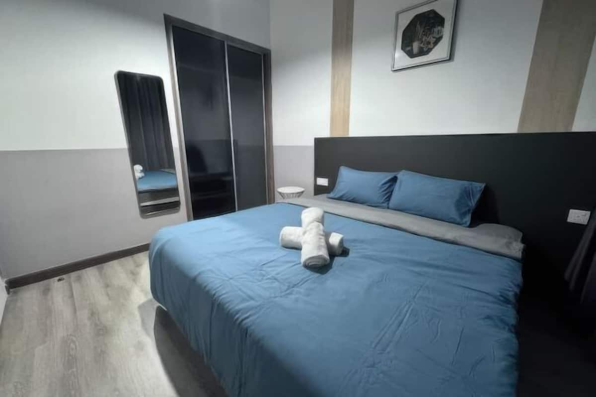 A bedroom with a bed, a nightstand, a chair, a wardrobe, and a framed picture on the wall.