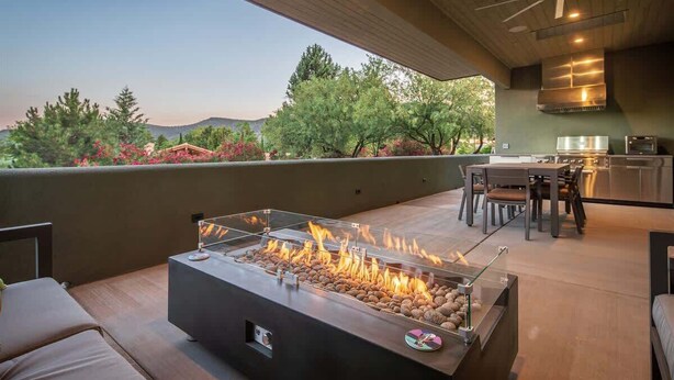 An outdoor patio with a fire feature, seating, a table, and a kitchen area.