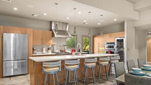 A modern kitchen with stainless steel appliances, a central island with bar stools, and a dining area with a table and chairs.