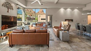A spacious living room with a large leather sofa, a dining area with chairs, a fireplace, and a view of the outdoors.
