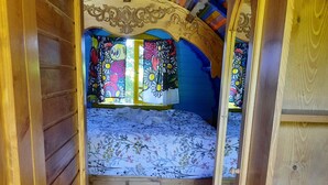 Une pièce confortable et compacte, avec un lit, un petit tabouret et un tapis coloré.