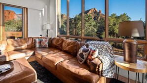 A room with a leather sofa, a lamp, and large windows with a mountain view.