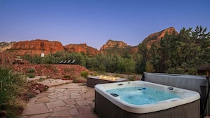 A hot tub in a landscaped outdoor area with a stone pathway, surrounded by red rock formations and trees.