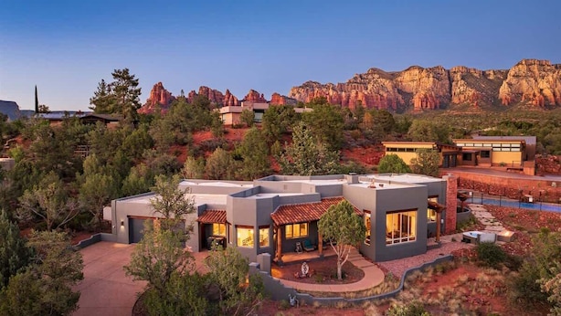 A modern house with multiple rooms, surrounded by trees and a mountainous backdrop.