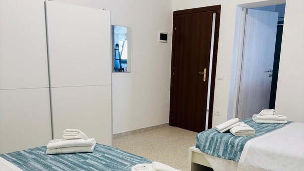 A hotel room with two single beds, a wardrobe, a door, and an air conditioning unit. - MMM HOME TRAIN STATION 1 (Mestre)