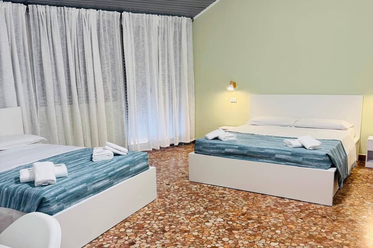 A hotel room with two beds, a desk, and a large window with curtains.