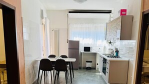 A compact kitchen with a refrigerator, microwave, and sink. There is a dining area with a table and chairs. The floor has a patterned tile design. - MMM HOME TRAIN STATION 1 (Mestre)