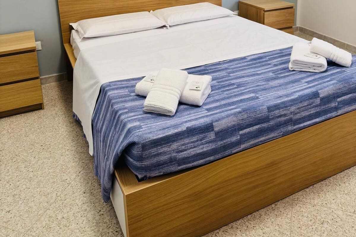 A neatly made bed with white linens and a blue striped blanket, two bedside tables with lamps, and a light blue wall.