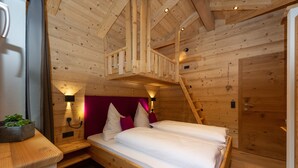 Een houten slaapkamer met een vide en een hoogslaper, een nachtkastje met een lamp, en een houten deur.