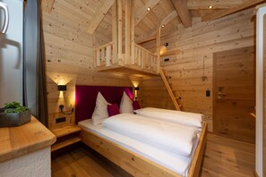 Une chambre dans une cabane en bois, avec un lit en mezzanine, une table de chevet avec une lampe et une porte en bois.