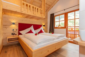 Une pièce aux murs lambrissés, avec un grand lit, une table de chevet, une lampe fixée au mur et une fenêtre avec des rideaux.