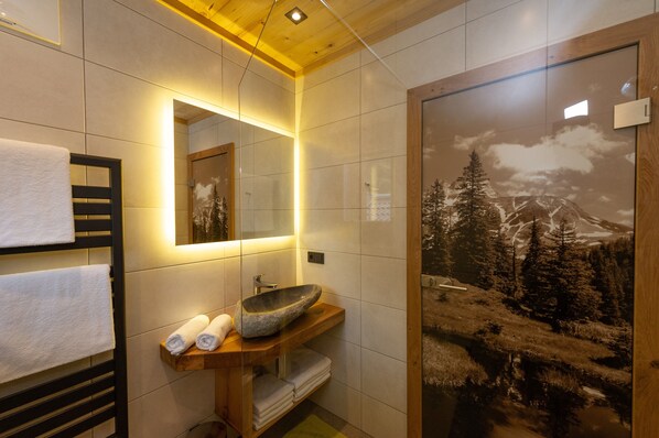 Un baño con tocador de madera, lavabo de piedra, espejo y toallero.