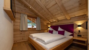 A wooden cabin bedroom with a bed, a window with curtains, a nightstand, and a wall-mounted light. - Apartment 'Deluxe 2' with Private Garden, Balcony and Wi-Fi (Großarl)
