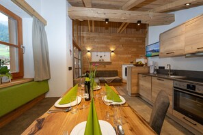 Un comedor con una mesa de madera dispuesta para dos, una cocina con armarios de madera y un televisor montado sobre la encimera.