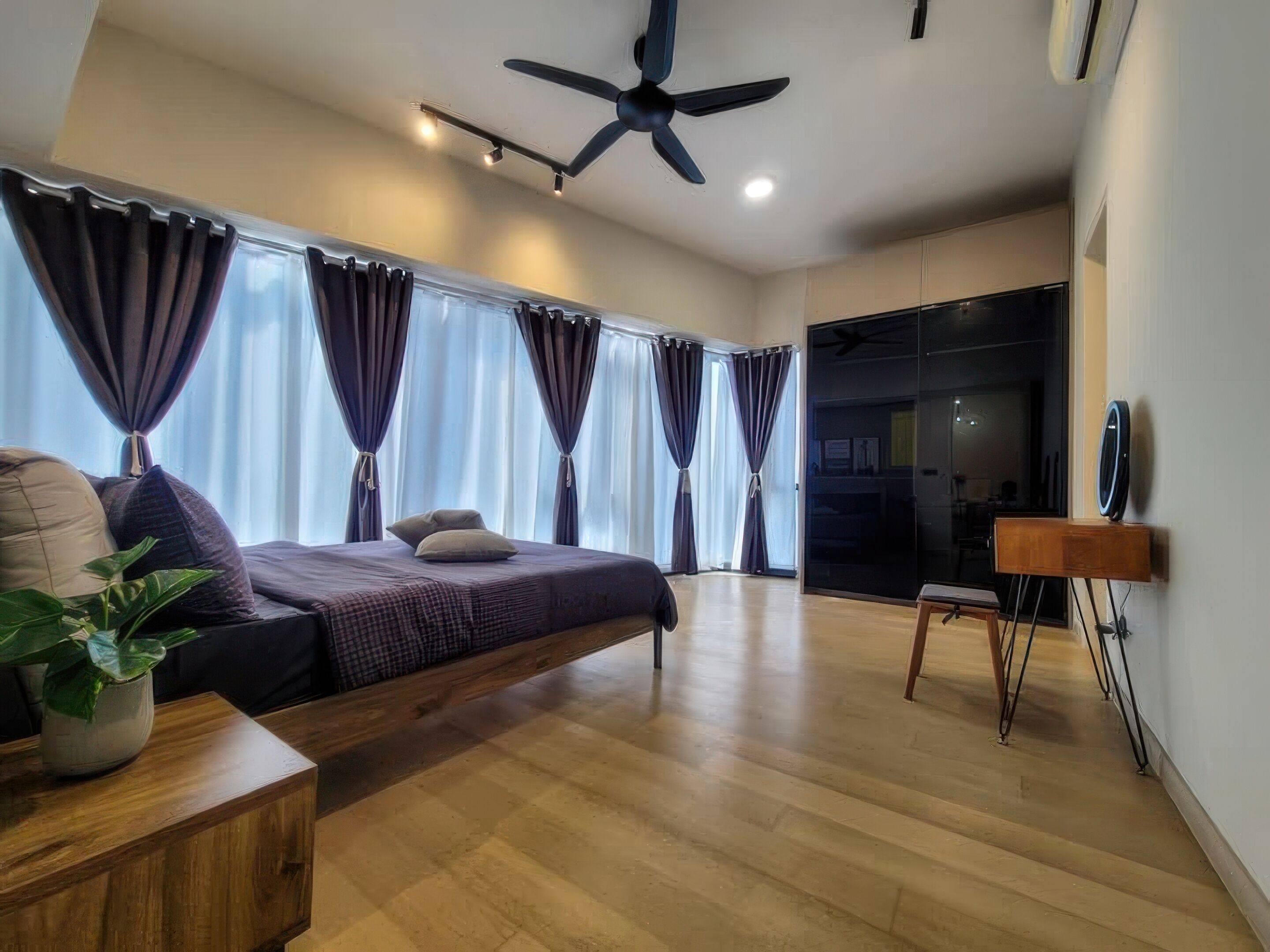 A modern bedroom with a bed, curtains, a ceiling fan, a wooden side table with a plant, and a TV on a stand.