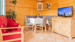 Ein Holzblockhaus-Innenraum mit Esstisch, Stühlen, einem Fernseher und einem Schrank.