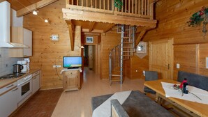 A wooden cabin interior with a kitchen, dining area, and a staircase leading to a loft. - Apartment 'Schuhflicker' with Private Garden, Balcony and Wi-Fi (Großarl)