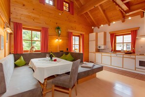 Een houten interieur met een eethoek, keuken en een groot raam met gordijnen.