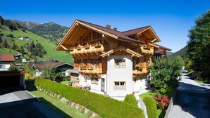 A two-story wooden house with balconies, surrounded by greenery and a mountain backdrop. - Apartment 'Schuhflicker' with Private Garden, Balcony and Wi-Fi (Großarl)