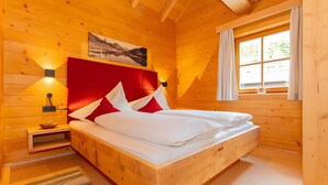 A wooden room with a bed, a nightstand, a wall-mounted lamp, and a window with curtains. - Apartment 'Schuhflicker' with Private Garden, Balcony and Wi-Fi (Großarl)