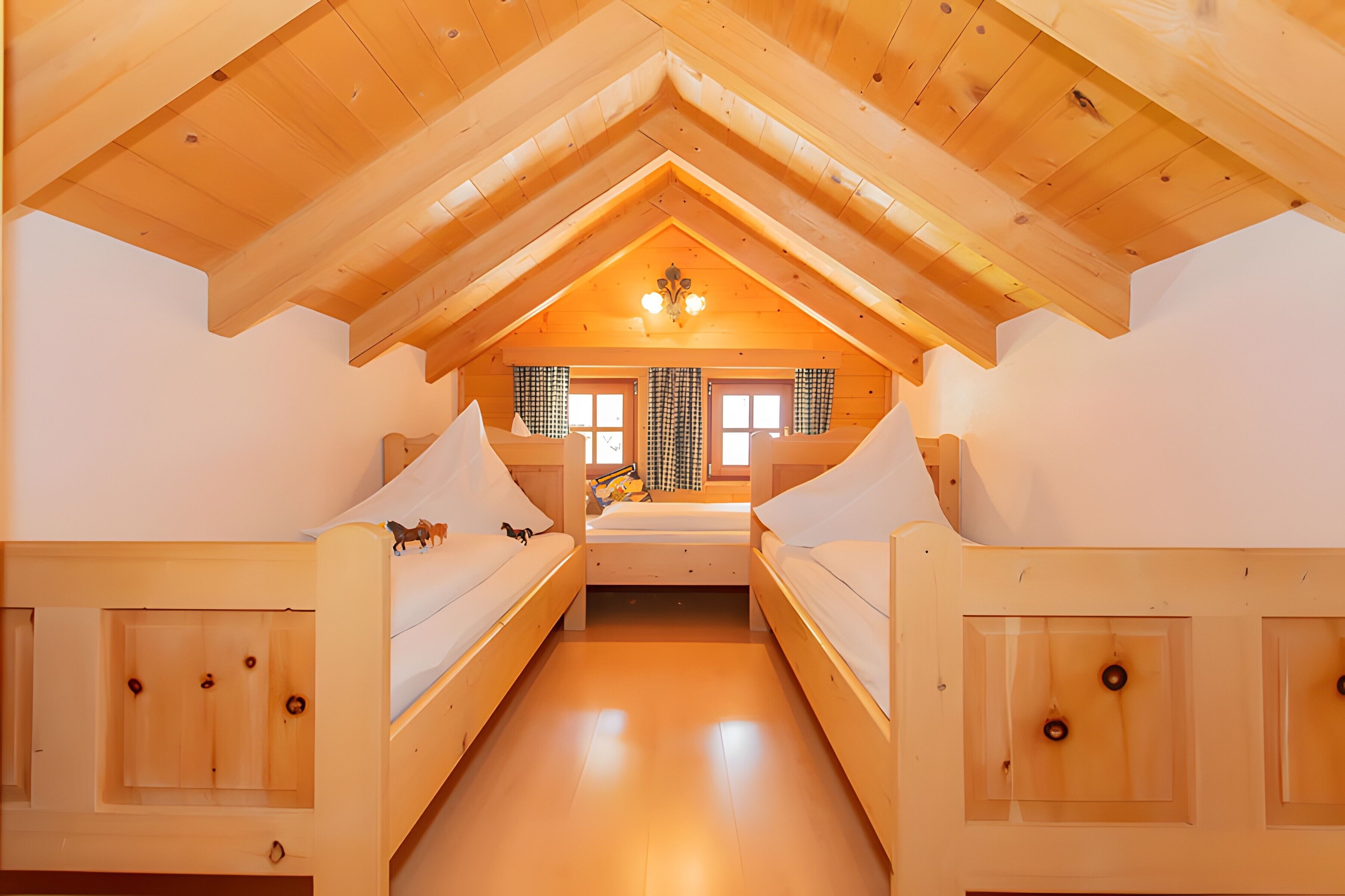 A wooden interior with a high ceiling, bunk beds, and a central window.