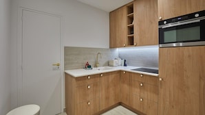 A compact kitchen with wooden cabinets, a built-in oven, and a white countertop. - Superb Apartment in the Heart of Paris (Paris)