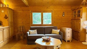 A cozy cabin interior with a sofa, a small table, a window, wooden walls, and a fan.