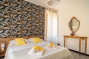 A hotel room with a bed, a wooden headboard, a nightstand, a mirror, and a wall with a leaf-patterned wallpaper. - I COLORI DELLA SICILIA NOBLESSE (Caltagirone)
