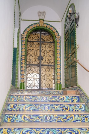 A staircase with ornate blue and yellow tiles leading to a door with a decorative metal gate. - I COLORI DELLA SICILIA NOBLESSE (Caltagirone)