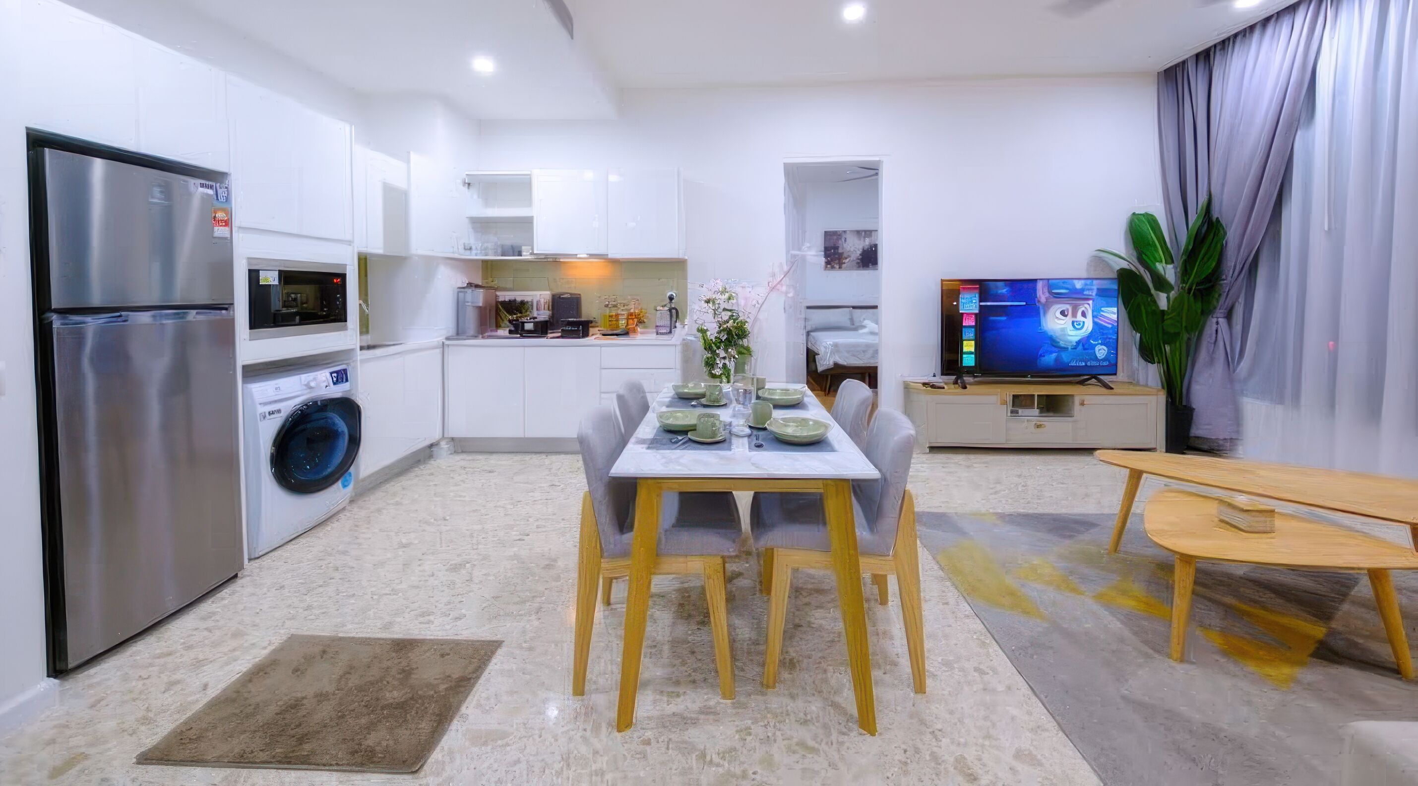 Una cocina moderna con lavadora integrada, un comedor con mesa para cuatro personas y un televisor sobre un mueble.