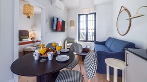 Ein modernes Wohnzimmer mit einem blauen Sofa, einem Essbereich mit einem schwarzen Tisch und karierten Stühlen sowie einem an der Wand befestigten Fernseher.