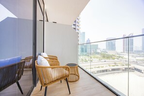 A balcony with wicker furniture and a glass railing overlooking a cityscape. - Bloomfields Fabulous STU In Al Maryah  (Abu Dhabi)